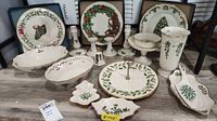 Full view of 18-piece Lenox Christmas serveware set displayed including plates, candle holders, bowls, vases, and serving platters featuring holly and holiday motifs