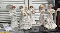 Six handcrafted Lenox lady figurines arranged on a glass shelf, showcasing their vintage styled dresses and accessories.