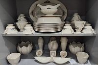 Third shelf showing Lenox Rutledge plates, bowls, cups, saucers and serving pieces with scalloped edges and floral motif.