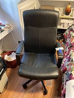 Front view of black rolling swivel office chair showing cushioned seat, armrests, and adjustable height lever.