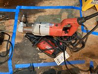 Top view of two electric drills, one Milwaukee and one Hilton SD 45, placed on a wooden surface with power cords visible.