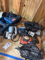 Wide view of six power tools on wooden shed floor including RYOBI reciprocating saw, sanders, saws