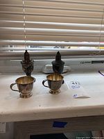 Photo showing two weighted sterling silver shakers and two mini tea cups placed on a windowsill under natural light.