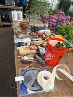 View of assorted painting supplies, hand tools and accessories arranged on a wooden table outdoors.