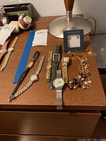 Overview of six wristwatches laid out on wooden surface alongside sterling silver earrings and two pieces of costume jewelry.