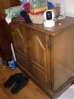 Front and side view of a brown wooden cabinet with two paneled doors and brass hinges, showing some scratches and wear.