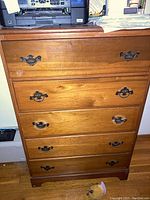 Front view of the wooden chest of drawers showing five drawers with metal pull handles and scratches on the wood surface.