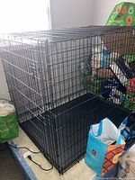 Full view of large collapsible metal wire pet crate with black plastic tray insert at the base, surrounded by pet supplies.