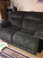 Front angled view of dark gray La-Z-Boy reclining loveseat showing fabric texture, armrest, and back cushions.