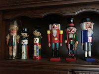 Full view of all five nutcrackers and one doll lined up on a wooden shelf.
