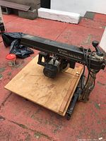 Photo of Black & Decker radial arm saw showing full saw with wooden base on a red concrete floor.
