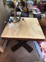 Close-up of one side table showing the light beige onyx top with scratches and carved wooden trim on edge. Wooden cross-legged base with dark finish visible.