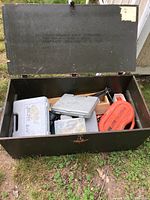 Open military foot locker with labeled stencil on lid, showing multiple tool cases and items inside.