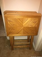 Four wooden TV trays stacked with foldable wooden legs, showing wood grain pattern on tray tops