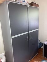 Full view of a dark-paneled particle board wardrobe with two doors and metal handles, framed with light gray trim and metal corner brackets.