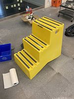 Full side view of the yellow safety chair with steps, showing anti-slip strips on the step surfaces and a cut-out handle side for grip