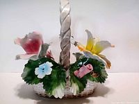 Front left angle view of porcelain Capodimonte flower basket sculpture highlighting pink rose, blue flower, green leaves, and twisted handle.