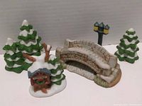 View of all five ceramic Christmas village pieces from front angle showing house, bridge, lamp, and trees.