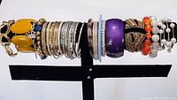 Photo of all 19 assorted costume jewelry bracelets displayed on a black display stand, showing variety of styles and colors