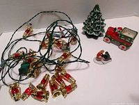 Lot overview showing red lantern light strand, green ceramic Christmas tree, Santa in red truck figurine, and couple skiing figurine.