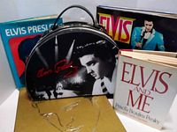 Photo showing black Elvis Presley purse with black and white photo and cursive signature, Elvis records, cassette tapes, and 'Elvis and Me' book.