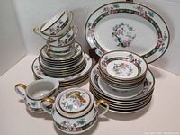 Full view of all items stacked together showing cups, plates, bowls and serving items with floral and gold decoration.