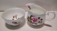 Fine china creamer and sugar bowl both decorated with pink rose floral designs and gold trim shown from front angle