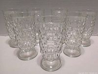 Seven clear glass juice glasses with cube textured pattern, shown from angled front view