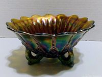 Side-angle view showing the iridescent finish and scalloped edge of the carnival glass bowl with ornate embossed patterns and curled feet.