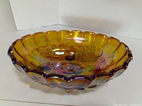 Top and inside view of amber carnival glass oval dish showing scalloped edges and floral embossed pattern with marigold iridescence.