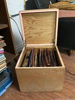 Open ottoman style storage case filled with multiple vintage vinyl records and 45s