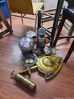 Photo showing medieval armor style figurine with shot glasses, brass sword and shield, metal and glass ashtrays, and an ice bucket on floor.
