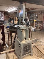 Front-right angled view of the wood cutting band saw set in a cluttered basement with other woodworking equipment and tools.