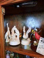 Ceramic bird figurines including white Capodimonte swan and cranes, Franklin Mint swan with raised wings, and painted wood bird figurines in shelf