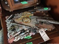 Top view photo showing multiple miniature cannon models placed on a table, varying in size and material including brass, silver, and wood.