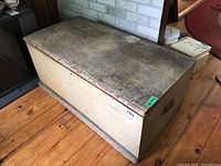 Front and top view of vintage wooden chest showing wear and metal handle on side.