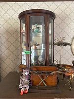Front view of wooden curio cabinet showing glass shelves with figurines inside and pipe stand with pipes outside.