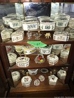 Wooden display case with mirrored back and glass front showing porcelain trinket boxes, floral patterns, music boxes, small glass dish, and elephant figurine inside.