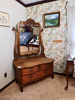 Front view of antique wood dresser with attached mirror showing detailed carvings, four drawers with metal handles, some surface wear.