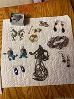 Full view of costume earrings and amethyst bracelet and earrings on white paper towel, displayed on wooden table.