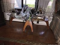 Front view of oval glass top and sculptural wood base with accessories on top (not included)