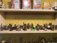 Shelf with more than 20 miniature vintage metal pencil sharpeners shaped like antique stoves, steam engines, gramophones, and telephones.
