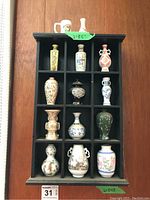Full view of the black wooden display case holding 12 miniature porcelain vases and a mug.