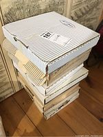 Stack of original packaging boxes for collector plates, showing a total of about seven boxes stacked on a wooden floor.