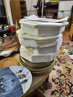 Stack of collectible plates with Styrofoam packing pieces on top, plates featuring detailed train scenes with gold trim.