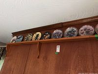 Shelf showing a row of 8 decorative collector plates featuring different pictures, arranged side by side with diverse art themes.