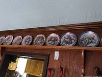 Set of 8 collector plates arranged on a shelf showing variety of floral designs and different decorative borders.
