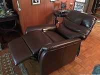 Brown faux leather electric recliner in reclined position showing extended leg rest and padded armrests.