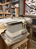 Side view of the Ryobi oscillating spindle sander showing unit on table with sanding drums inserted and manual on top.