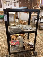 Full view of black metal trolley with two shelves holding various saw blades and miscellaneous items.